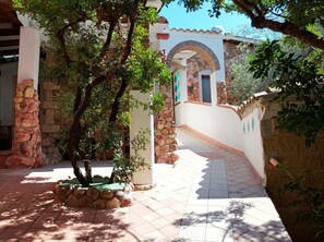 A courtyard with stone walls, a tiled floor, and a tree providing shade.