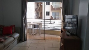 A living room with a sofa, a TV, a small table, and chairs. There is a balcony with a view of buildings and a fence. - Temporada Royal Park Caldas Novas 3q (Caldas Novas)