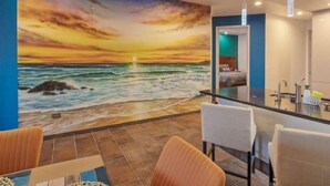 A room with a sunset mural on the wall, a bar area, and a seating area with chairs. - Gorgeous Ocean Front Resort J 107 (Puerto Peñasco)