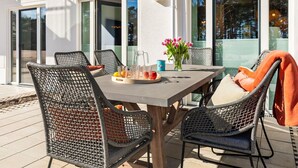 An outdoor patio with a table and wicker chairs, a vase with flowers, and a glass pitcher.