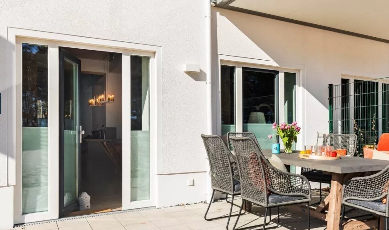 An outdoor patio with a table and chairs, a sliding glass door, and a small garden area with flowers.