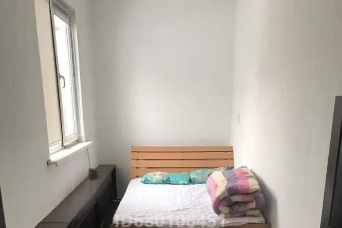 Una habitación pequeña y estrecha con una cama individual, cabecera de madera y una ventana.