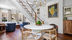 Amplia sala de estar con una mesa redonda blanca, sillas de mimbre, un sofá azul y una escalera de madera.
