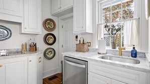 Una cocina con armarios blancos, encimera de mármol, lavavajillas y platos decorativos en la pared.