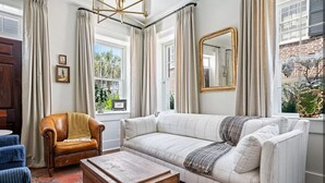 Una sala de estar con un sofá blanco, una mesa de centro de madera, un sillón de cuero y un espejo grande.