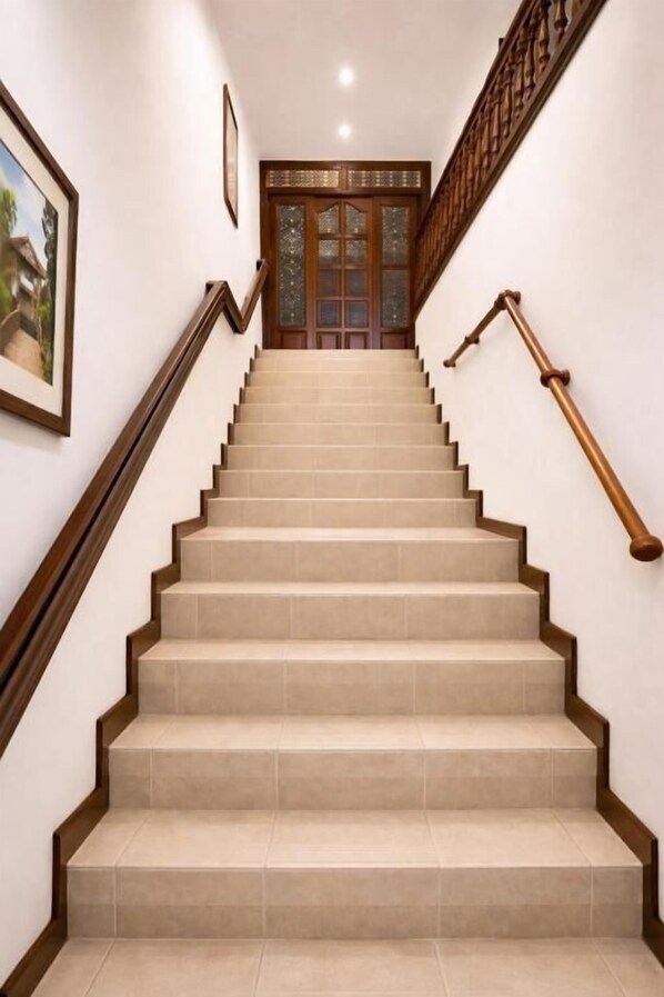 A staircase with wooden handrails and beige steps leading to a door with glass panels. - Hospedaje Camino Real  (Salento)