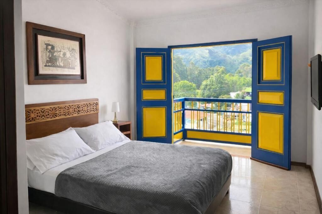 Une chambre à coucher avec un lit, une table de chevet, un tableau encadré et un balcon doté de balustrades jaunes et bleues.