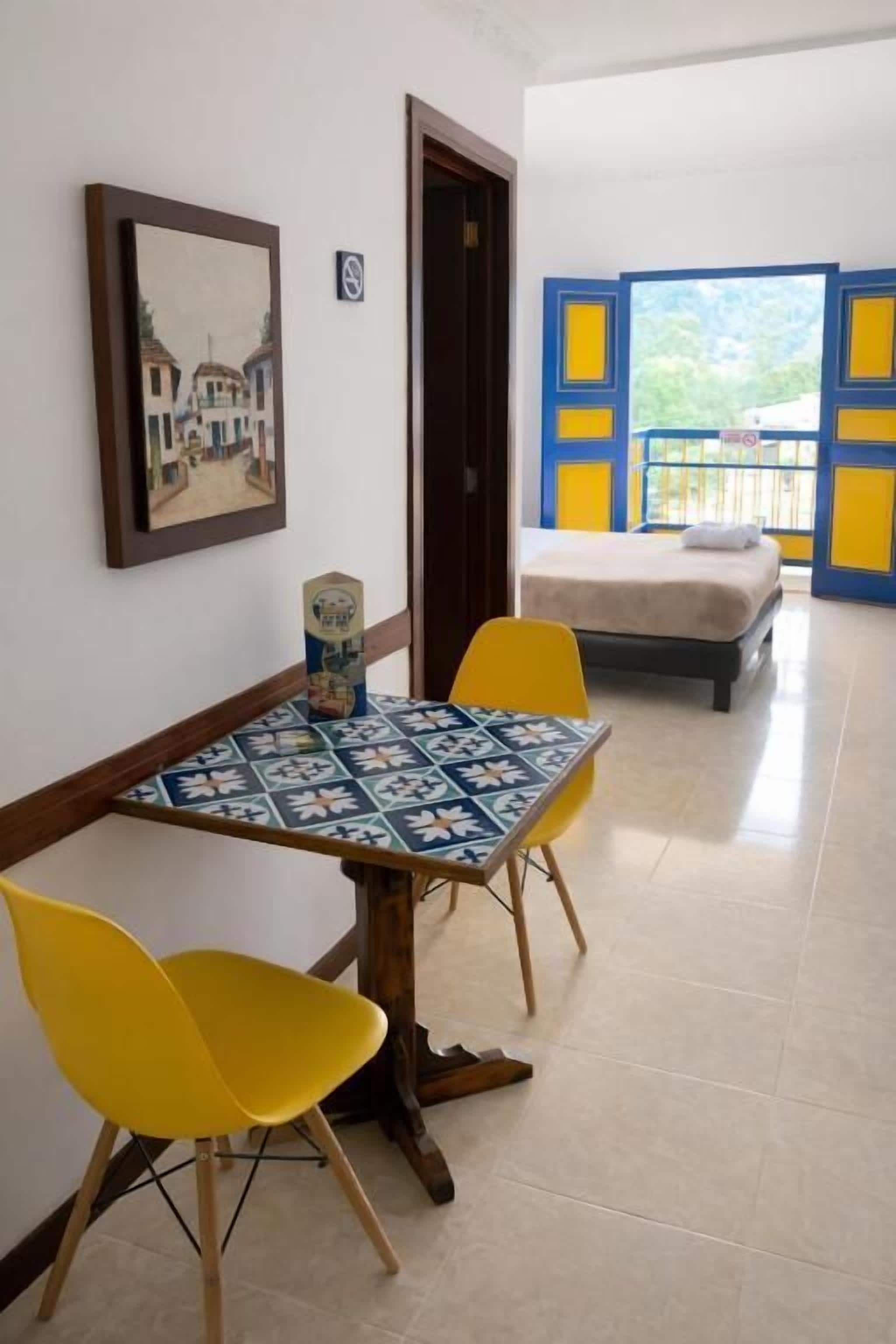 Una habitación con cama, una mesa con sillas, un cuadro en la pared y vistas a través de una ventana.
