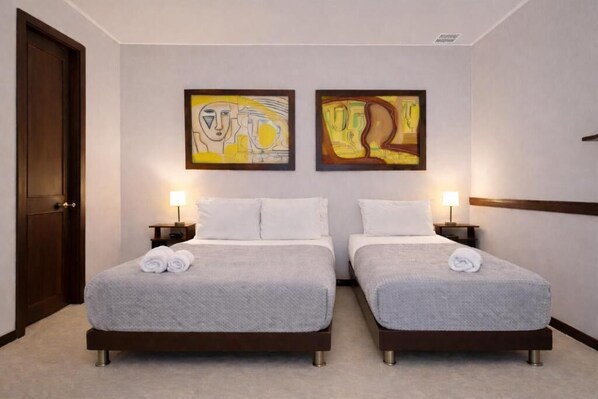 A hotel room with two beds, a door, and two abstract paintings on the wall. - Hospedaje Camino Real (Salento)