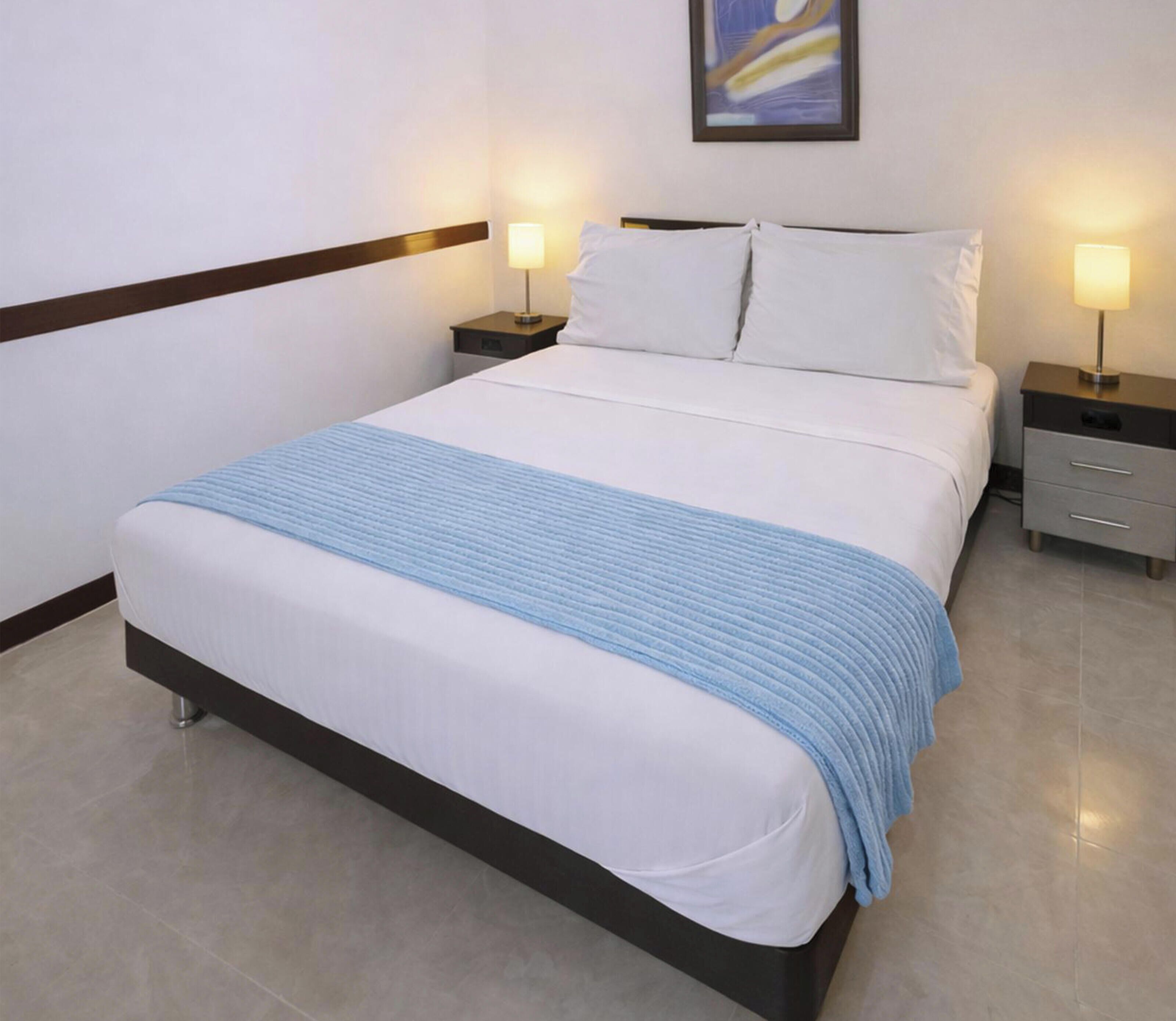 A hotel room with a bed, two bedside tables, and a wall-mounted lamp.