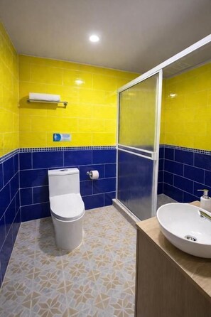 Ein Badezimmer mit gelben und blauen Fliesen, einer Toilette, einem Waschbecken und einer Duschkabine.
