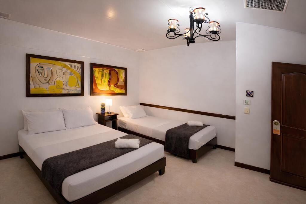 Una camera d'albergo con due letti, un lampadario e due quadri alle pareti.