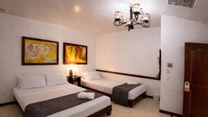 A hotel room with two beds, a chandelier, artwork on the walls, and a door. - Hospedaje Camino Real  (Salento)
