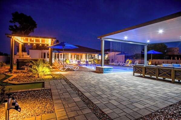 An outdoor pool area with lounge chairs and umbrellas, surrounded by a covered patio with seating.