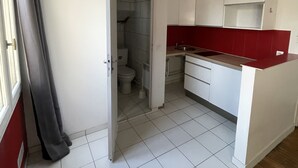 A compact kitchen with white cabinets, a red countertop, and a tiled floor. - Appartement Cosy au Pied de La Défense (Courbevoie)