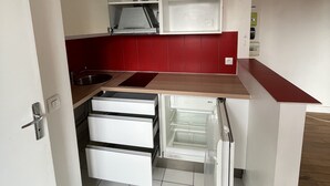 A compact kitchen with white cabinets, a stainless steel range hood, and a built-in dishwasher. - Appartement Cosy au Pied de La Défense (Courbevoie)