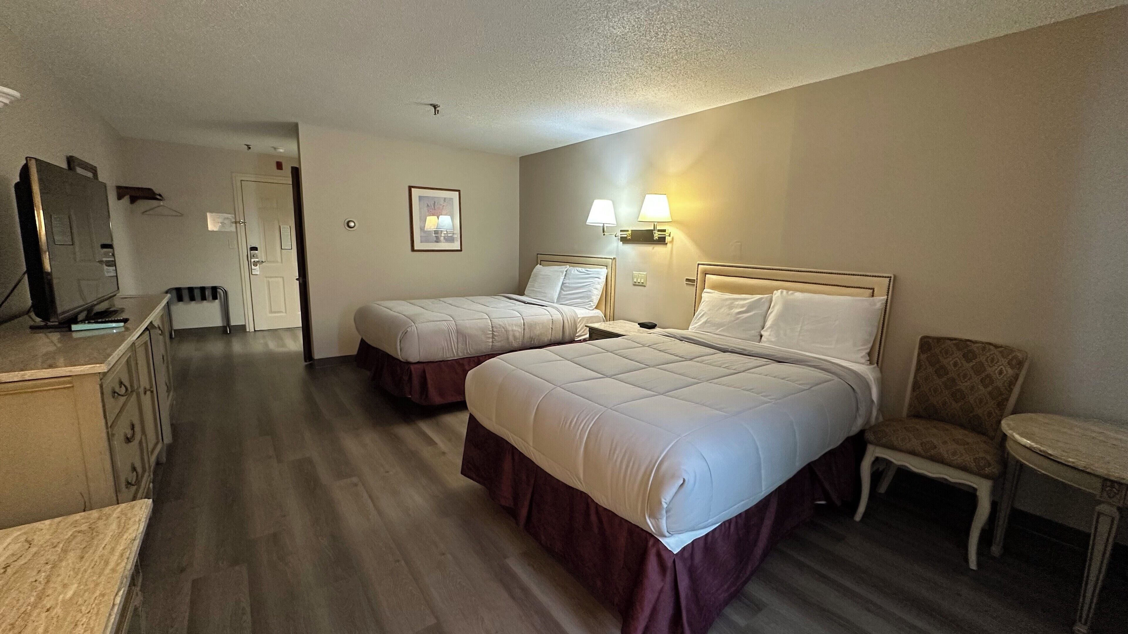 A hotel room with two beds, a desk, a chair, and a television.