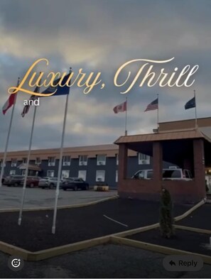A hotel entrance with flags, a parking lot, and a building in the background.