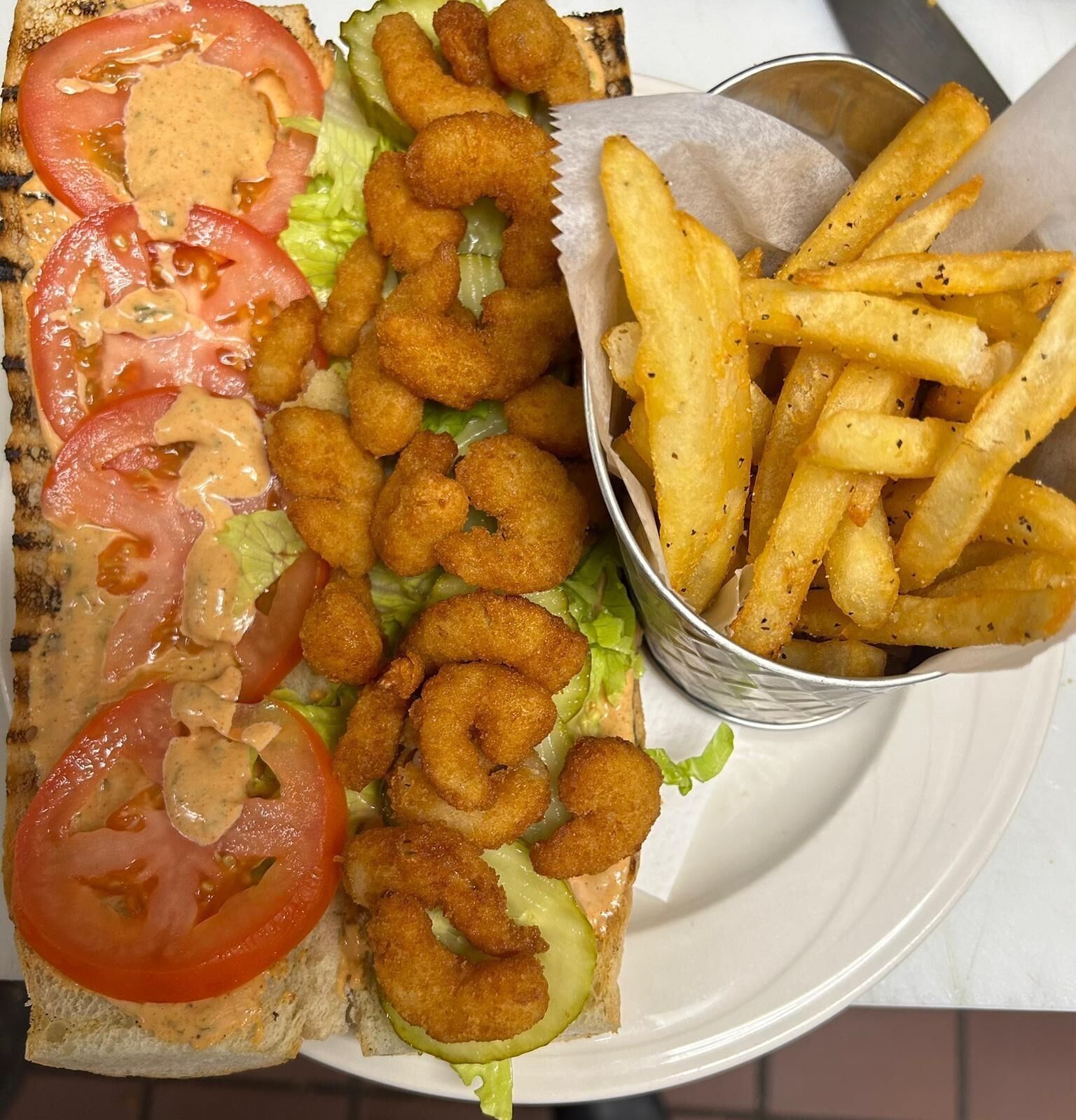 A sandwich with lettuce, tomato, and a creamy sauce, accompanied by a side of French fries.
