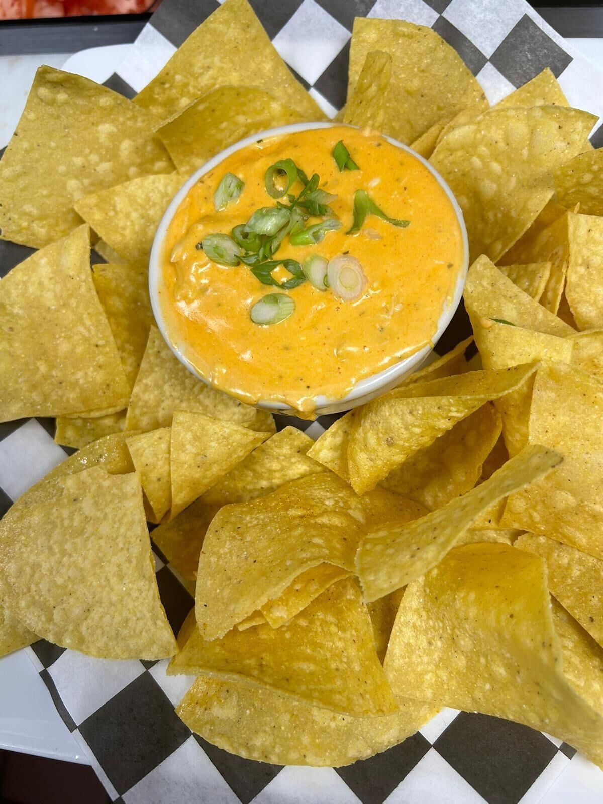 Un cuenco de salsa de naranja rodeado de totopos sobre un papel cuadriculado.