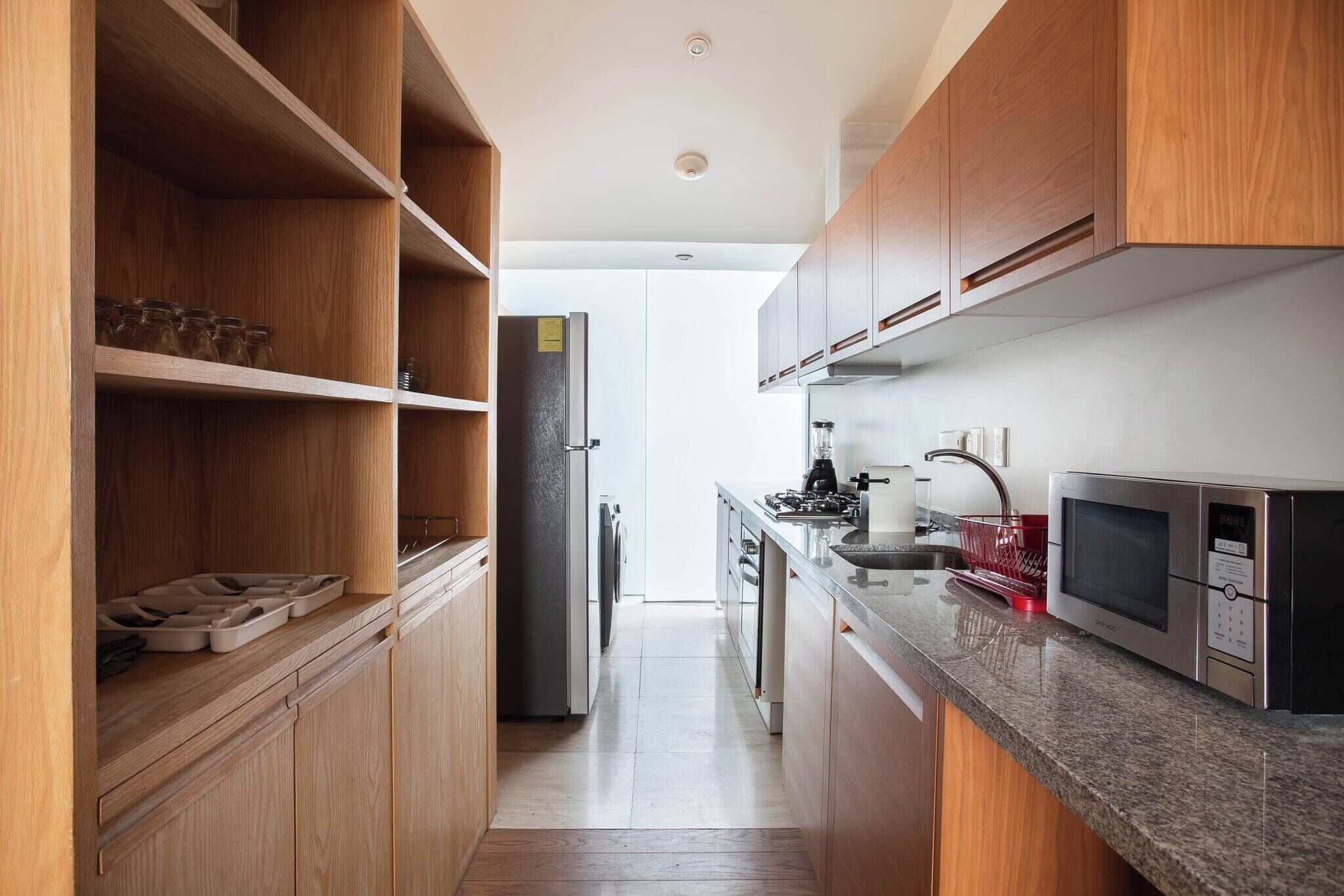 Eine moderne Küche mit Holzausstattung, einem Edelstahlkühlschrank, einer Mikrowelle und einem Spülbecken.