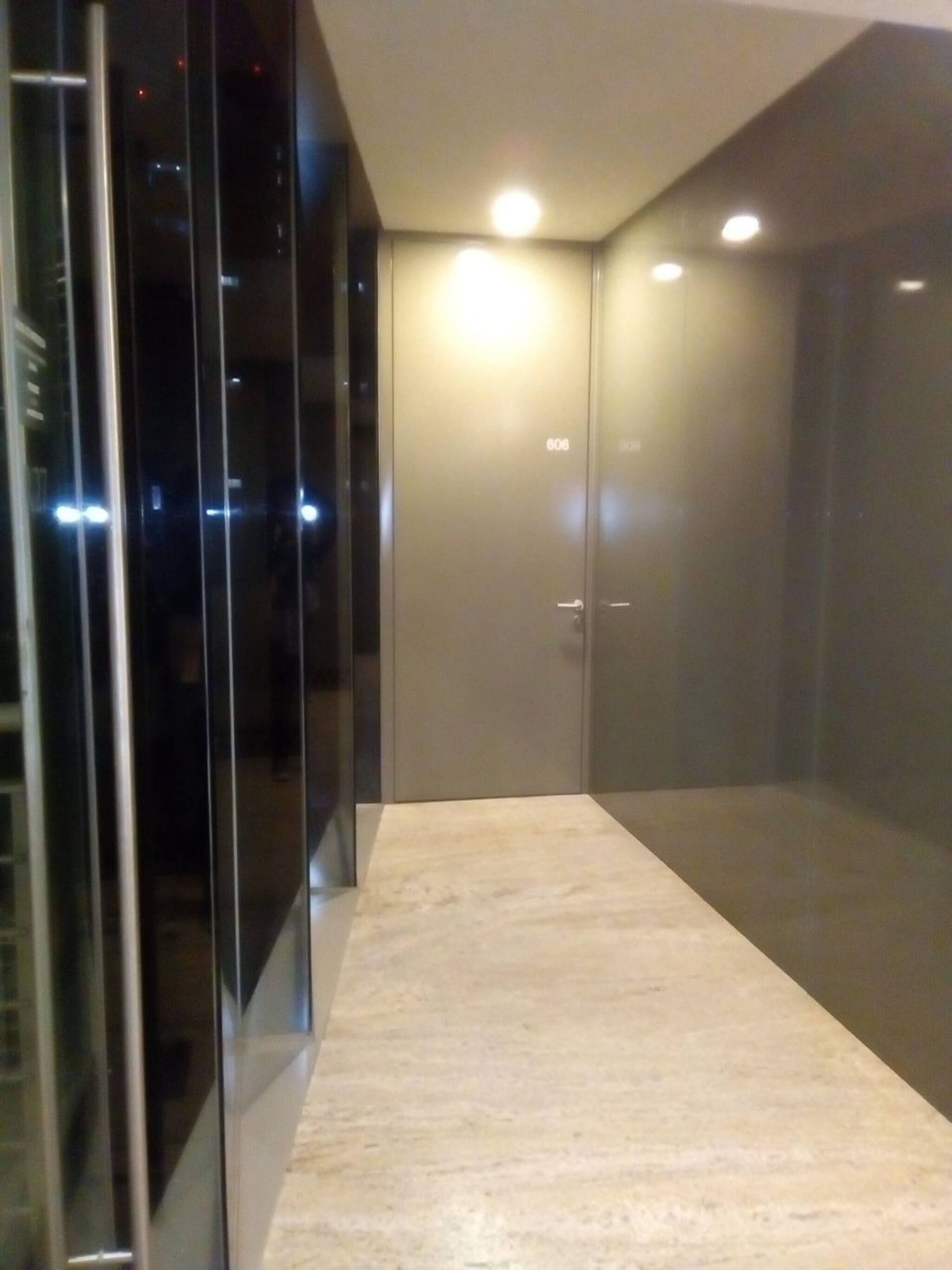 A modern, dimly lit hallway with a glass door marked '606' and a marble floor.
