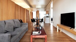 A modern living room with a grey sofa, wooden panel walls, a dining area, and a TV on the right. - Incredible Apartment Reforma 3rooms Great Location (Mexico City)