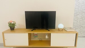 A wooden TV stand with a flat-screen TV, two drawers, a small potted plant, and a decorative item.