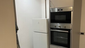 A compact kitchen with a built-in oven, a refrigerator, and a microwave.