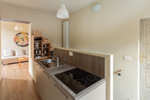 A compact kitchen with a stove, wooden shelves, and a dining area with a sofa and table.