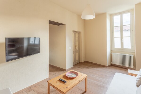 A modern living room with a flat-screen TV, a wooden coffee table with a bowl and remote, a white sofa, and a large window with a view.