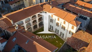 An aerial view of a building with a courtyard, surrounded by other buildings with red-tiled roofs. - PM7        (Castello Cabiaglio)