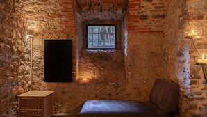 A cozy room with a brick wall, a small window, a bench, and a floor lamp. - PM7        (Castello Cabiaglio)