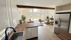 Cozinha moderna com bancada de madeira, eletrodomésticos de aço inoxidável e área de refeições com vista para o exterior.