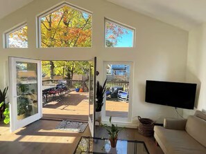 Een ruime woonkamer met een grote glazen deur naar een terras, een flatscreen televisie aan de muur en een comfortabele zithoek.