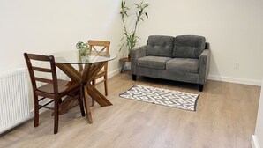 Uma sala de estar moderna com uma mesa de jantar de vidro, cadeiras de madeira, um sofá cinza e um tapete estampado.