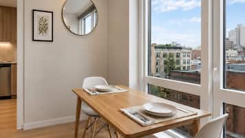 A modern dining area with a wooden table, white chairs, a round mirror, and a framed picture on the wall.