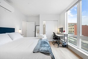 Una camera d'albergo con un letto grande, una scrivania con un computer e vista sulla città attraverso ampie finestre.