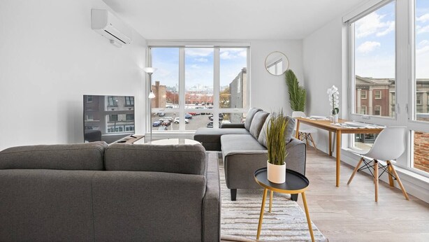 Una sala de estar moderna con un sofá gris, una mesita con una planta y un comedor con una mesa y sillas de madera.