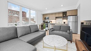 Un apartamento moderno con un sofá gris, una mesa de centro redonda de mármol y una cocina con armarios de madera y electrodomésticos de acero inoxidable.