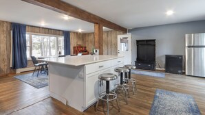 Eine moderne Küche mit Kochinsel, Barhocker, Kühlschrank und einem Essbereich mit Stühlen und Tisch.
