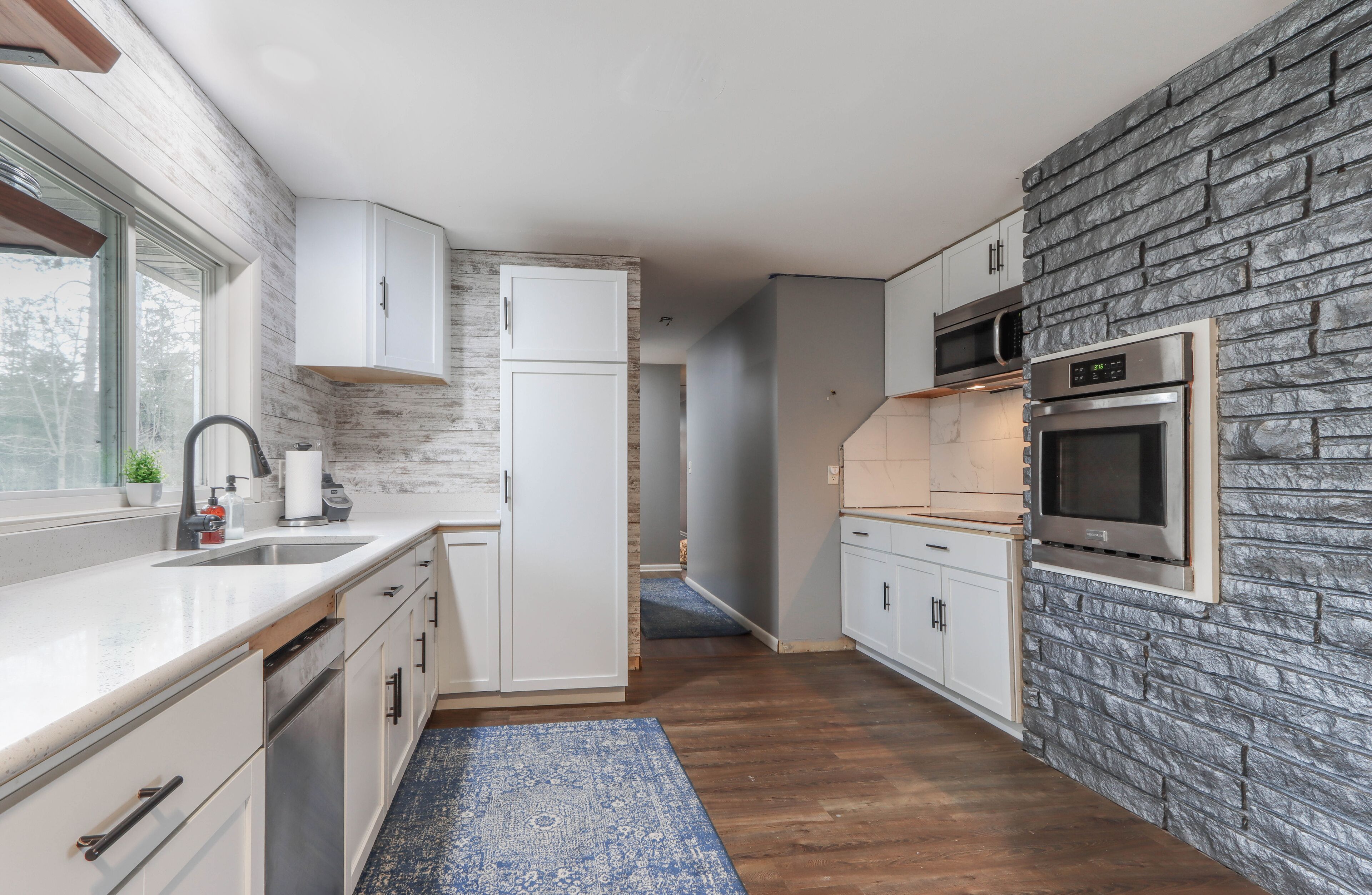 Una cocina moderna con armarios blancos, una pared de acento de piedra y electrodomésticos integrados.