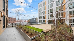 Un jardí a la terrassa amb gespa verda, jardineres i vista a un paisatge urbà.