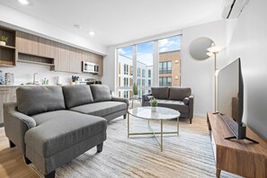 Un salon moderne avec un canapé d’angle gris, une table basse ronde et un téléviseur à écran plat posé sur un meuble en bois.