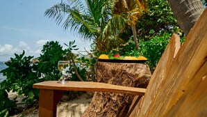 A wooden table with a glass of white wine and a fruit platter on a tree stump, surrounded by tropical foliage and a clear sky. - Wild Lotus Glamping (Bequia Island)