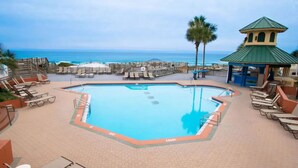 A swimming pool with a view of the ocean, surrounded by lounge chairs and a gazebo.