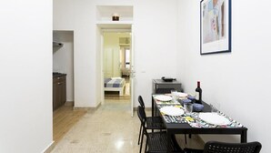 A narrow hallway leading to a dining area with a table set for two, a bed visible in the background, and a framed picture on the wall. - STAR POLITEAMA APARTMENT, IN CENTERideal for family or business trips. (PALERMO)