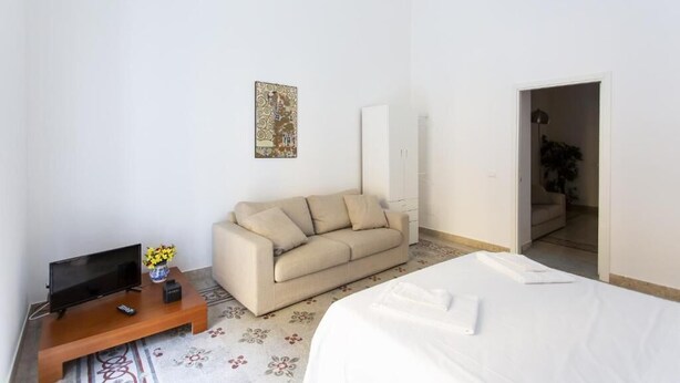 A hotel room with a bed, a sofa, a TV, and a painting on the wall. - STAR POLITEAMA APARTMENT, IN CENTERideal for family or business trips. (PALERMO)