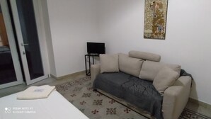 A room with a beige sofa, a flat-screen TV on a stand, a patterned rug, and a door leading to a balcony. - STAR POLITEAMA APARTMENT, IN CENTERideal for family or business trips. (PALERMO)