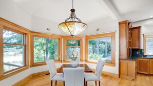 Un comedor amplio con una mesa y sillas de madera, ventanas grandes que ofrecen vistas a zonas verdes y armarios de madera.